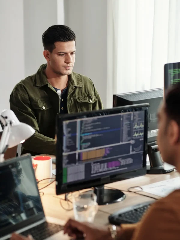 Two people at a desk with computers displaying code in a well-lit office.